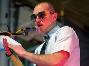 Charles Levesque in sunglasses and a tie speaking into a microphone.